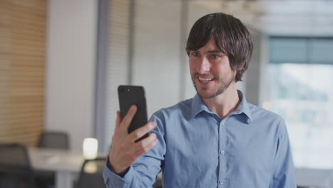 businessman having video chat on mobile phone call standing in modern open plan office