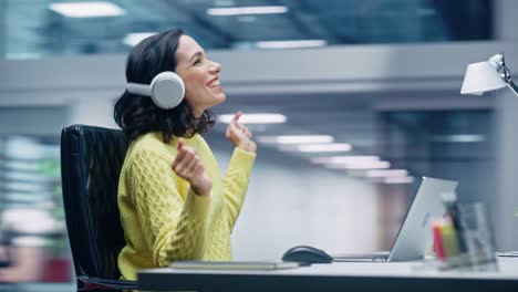 360 degree office: smiling hispanic businesswoman sitting at desk working on computer, wearing headphones, listening music, dances. she's happy, enjoys herself, having fun. moving around tracking shot