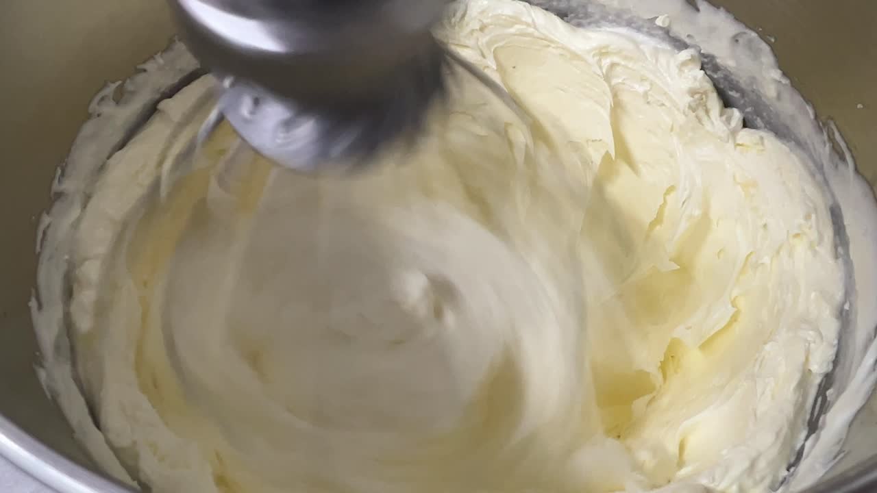 Tasty pastry making in progress, butter cubes added into whipped egg white, mixing in electric mixer, preparation for Swiss meringue buttercream