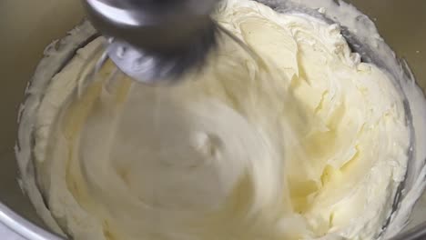 tasty pastry making in progress, butter cubes added into whipped egg white, mixing in electric mixer, preparation for swiss meringue buttercream