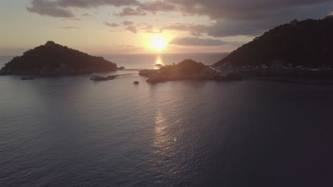 aerial view,pan right slowly over the blue ocean looking at the sunset on the horizon behind koh nang yuan islands at koh tao,thailand.