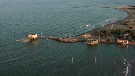 Aerial-shot-of-the-valleys-near-Ravenna-where-the-river-flows-into-the-sea-with-the-typical-fishermen's-huts-at-sunset