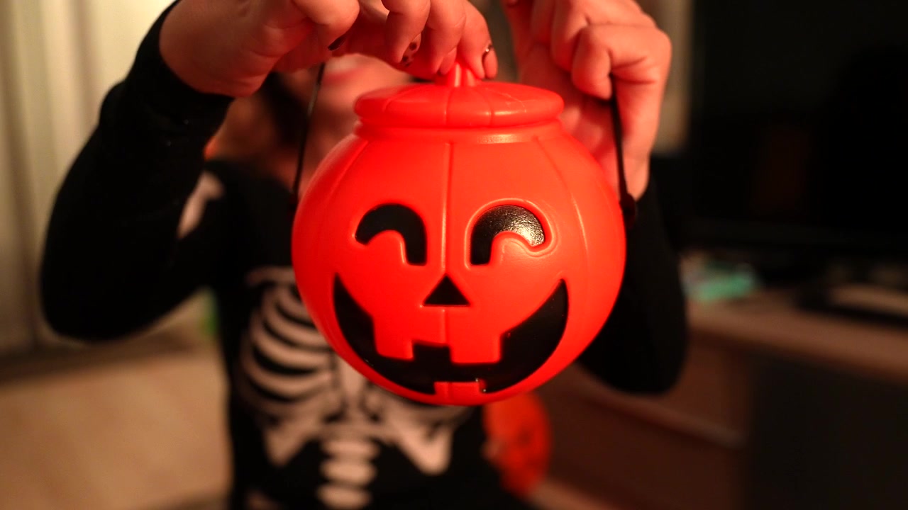 Woman in Skeleton Costume Opening a Plastic Pumpkin Halloween Candy Bucket