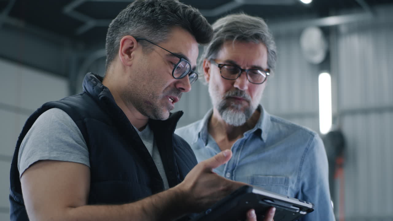 Two men discussing work in a garage using a tablet