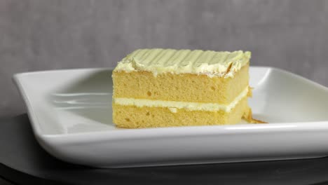 a slice of yellow frosted cake on a white plate