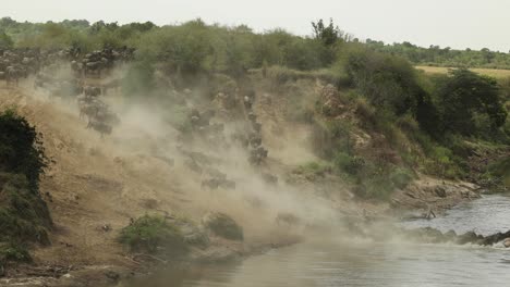 clip de cámara lenta de una manada de ñus corriendo por una pendiente polvorienta y hacia el río en el masai mara, kenia
