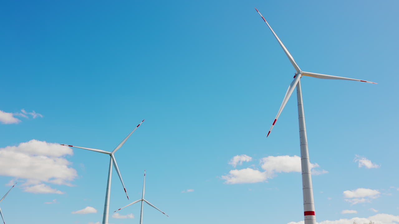 Several rotating turbines at daytime period. Blades spin at the backdrop of blue sky with little clouds. Low angle view.