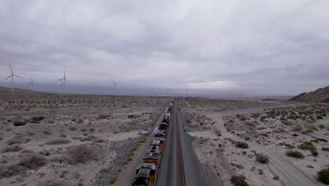 aerial drone footage of cargo train in palm springs desert with wind farms in the background, slow moving shot