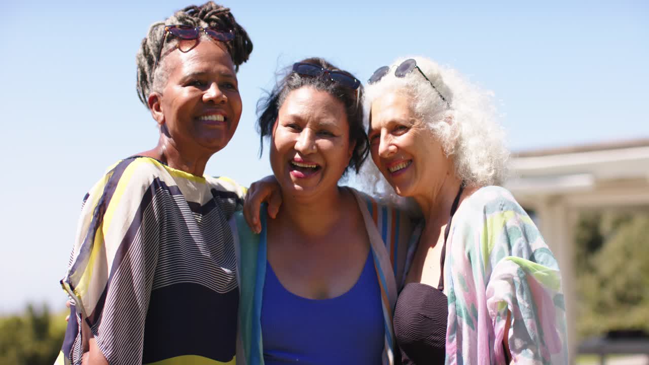 Un grupo diverso de amigas posando a la señal de la cámara en el parque, riendo, moviéndose y luciendo gafas de sol y trajes de baño.