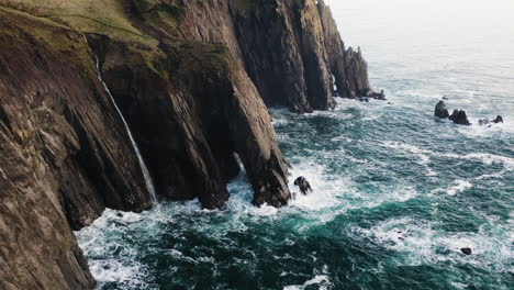 Flight-along-sheer-cliffs-on-Oregon-Coast,-over-rough-surf-of-Pacific-Ocean