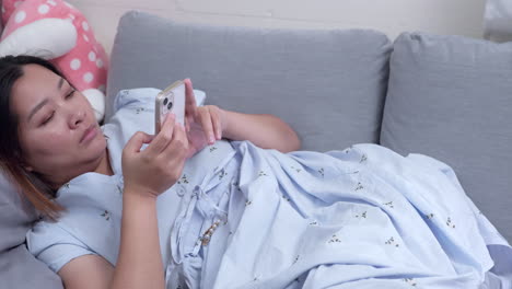 woman lying down on a couch while she is browsing her phone to check her messages on her social media