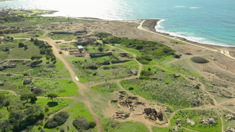 an overhead shot of the tombs of the kings, displaying the sprawling archaeological site with well-preserved ruins, greenery, and walking paths near the coastline