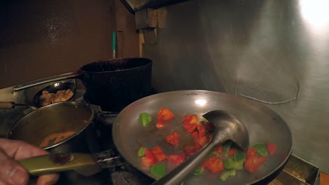 manos de cheque vertiendo aceite en una sartén de verduras y tofu al curry con llamas estallando hacia arriba durante la agitación