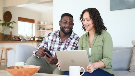 happy multiracial couple using laptop and smartphone at home, enjoying quality time together
