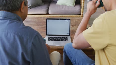 hombre bebiendo café mientras está sentado con su padre viendo video en una pantalla de computadora portátil en blanco con espacio de copia
