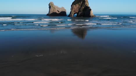 Perfekte-Wasserspiegelungen-Von-Zwei-Der-Torbogeninseln-Am-Wharariki-Strand-In-Der-Tasmanischen-See,-Puponga,-Neuseeland