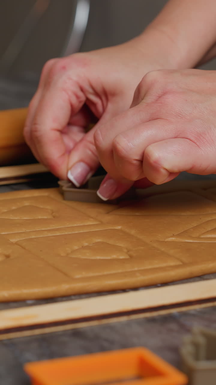 primer plano de una mujer usando un cortador cuadrado naranja en la masa, formando cuadrados limpios, rodillos y otras herramientas de horneado son visibles cerca en la encimera de mármol