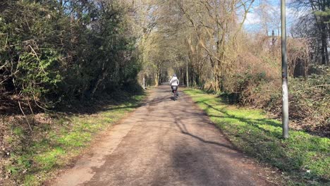 Woman-with-a-white-jacket-on-a-bicycle-goes-through-a-path-in-the-green-and-turns-left