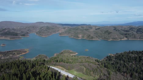 Volando-Sobre-La-Orilla-Del-Lago-Plastira-En-Grecia-Central-En-Una-Tarde-De-Primavera-Con-El-Sol-Proyectando-Largas-Sombras-|-4k