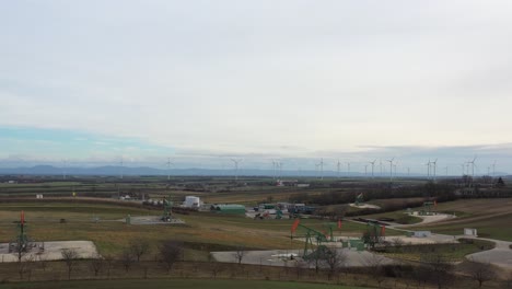 [drone]revealing shot of a scenery with multiple oil derricks moving and wind turbines in the background