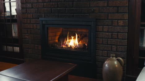 closeup of a gas fireplace lit inside of a home surrounded by brick in front of a dark wood coffee table