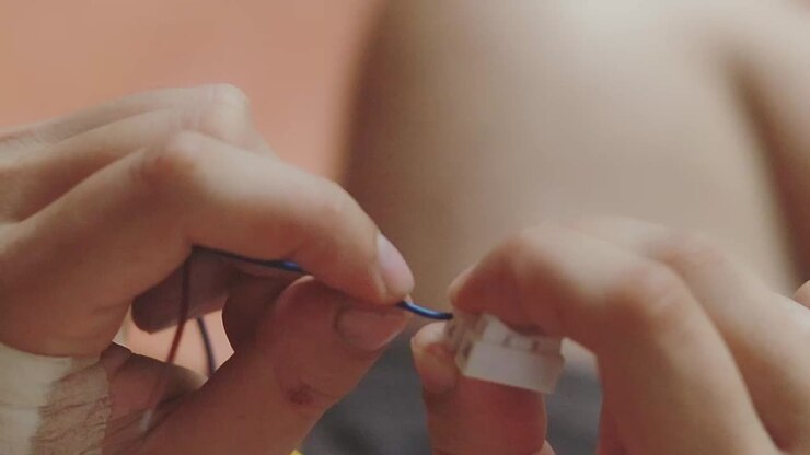 Close-up of hands connecting electric cable wires, showing delicate work and attention to detail, likely related to electronics