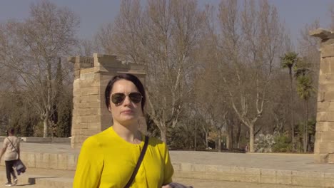 Young-tourist-woman-in-yellow-shirt-walking-past-the-Egyptian-monument,-Temple-of-Debod,-in-Madrid,-tracking-mid-shot