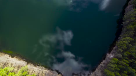 Blue-lake-with-shape-of-heart-with-clouds-reflected-on-water-with-trees-around