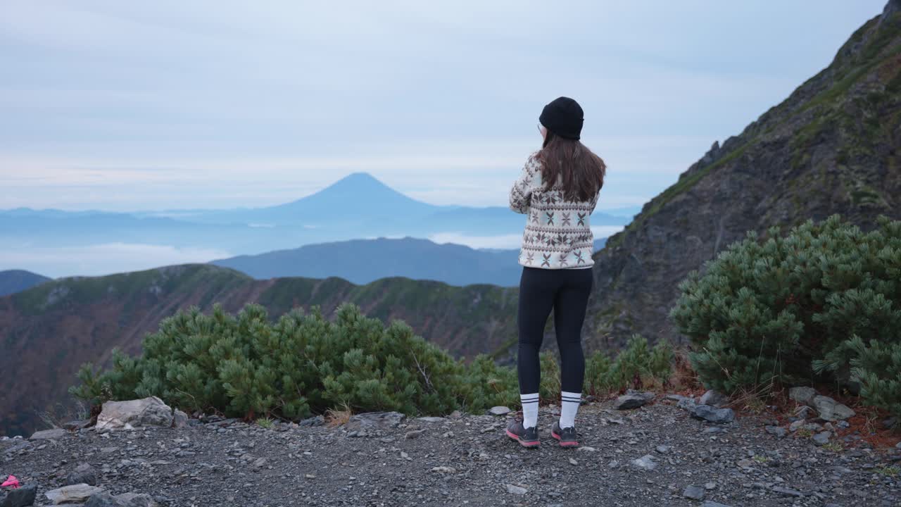 Young caucasian woman in beanie walking to a viewpoint looking at Mt. Fuji from Mt. Kitadake, Japanese Alps