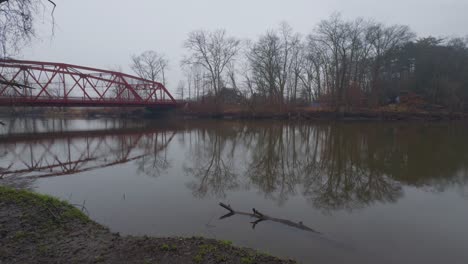 a small, picturesque arched red steel bridge, as seen from a little park, crossing a small river in upstate new york on a rainy, dreary, early-spring day