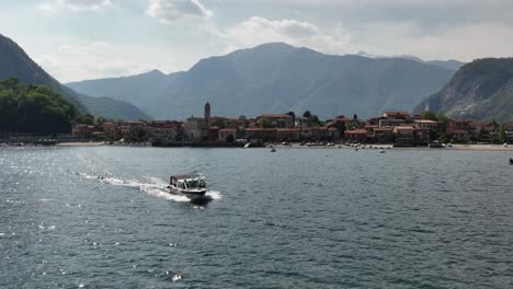 Low-aerial-shot-of-a-boat-pulling-out-of-a-marina-of-a-mountain-lake-with-a-villa-and-towering-mountains-in-the-background