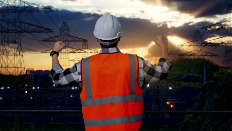 back view of a male engineer with safety helmet raising his hands celebrating while working near high voltage tower