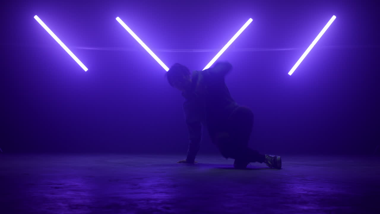 bailarina elegante bailando breakdance con ropa de calle en ultravioleta. hombre moviendo las piernas.