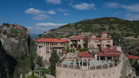 drone pulls back from monastery on steep cliffs in meteora, greece under bright daylight