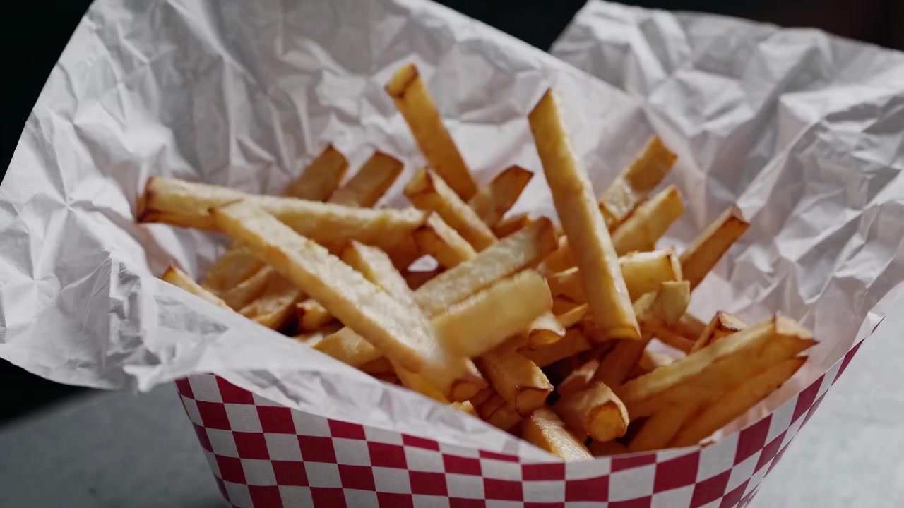 Hand Picking Up and Dropping Golden French Fries in a Basket
