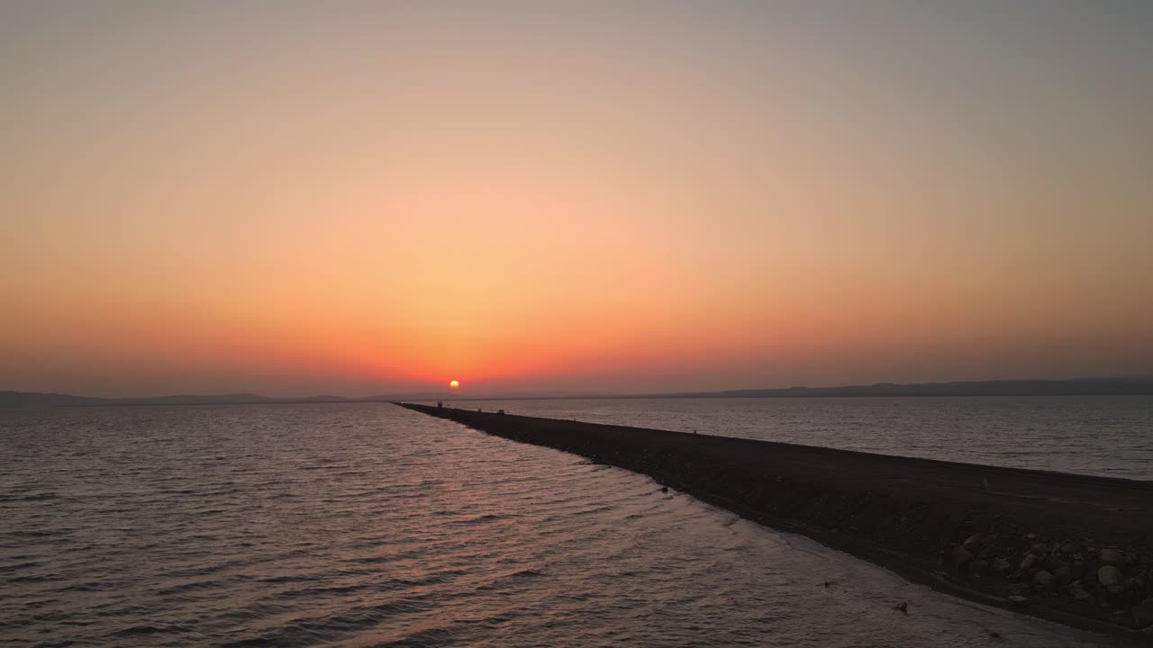 A stunning top drone view of a car cruising on the Road to Heaven in Kutch, Gujarat, a scenic highway flanked by the sea on both sides. The golden sunset reflects beautifully