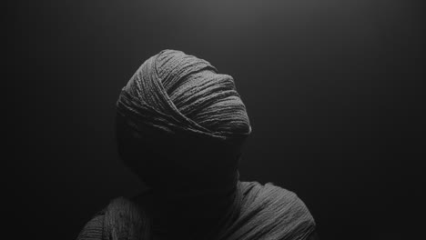 A mummy of a woman on a dark backdrop rises her head
