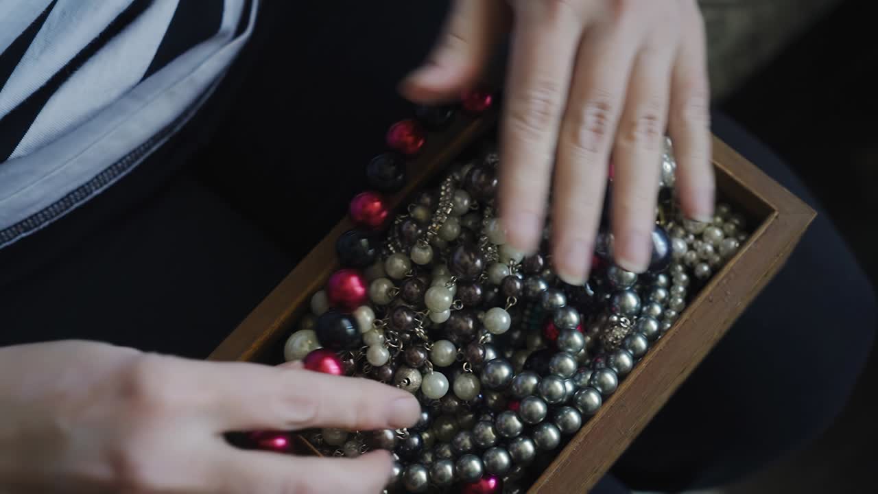 las manos de las mujeres apilan fuertemente collares y otras joyas en una caja de madera para almacenar.