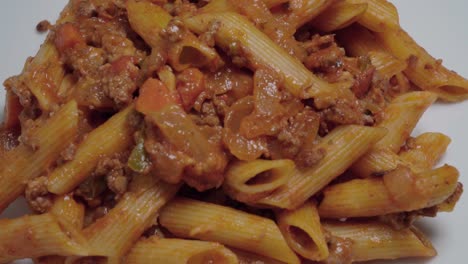 pasta bolognese with penne noodles on white plate, overhead pan right