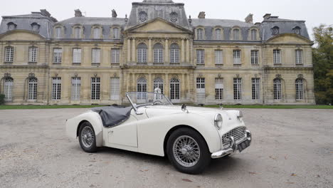 white vintage convertible parked in front of a grand chateau