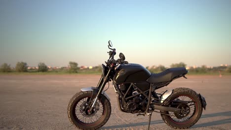 A-black-motorcycle-parking-on-the-ground-outdoors,-green-strip-of-trees-on-background