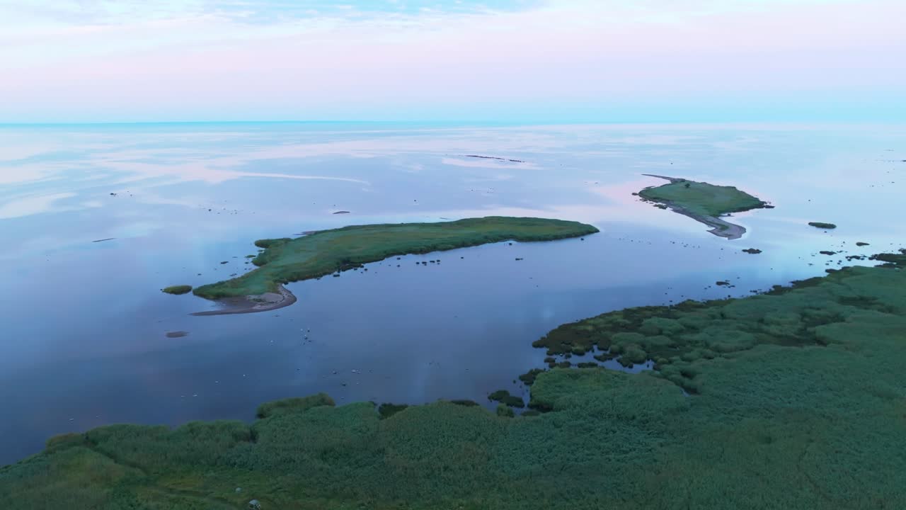 Flying above a calm sea and coastline and rotating shot around two small islands in the evening light
