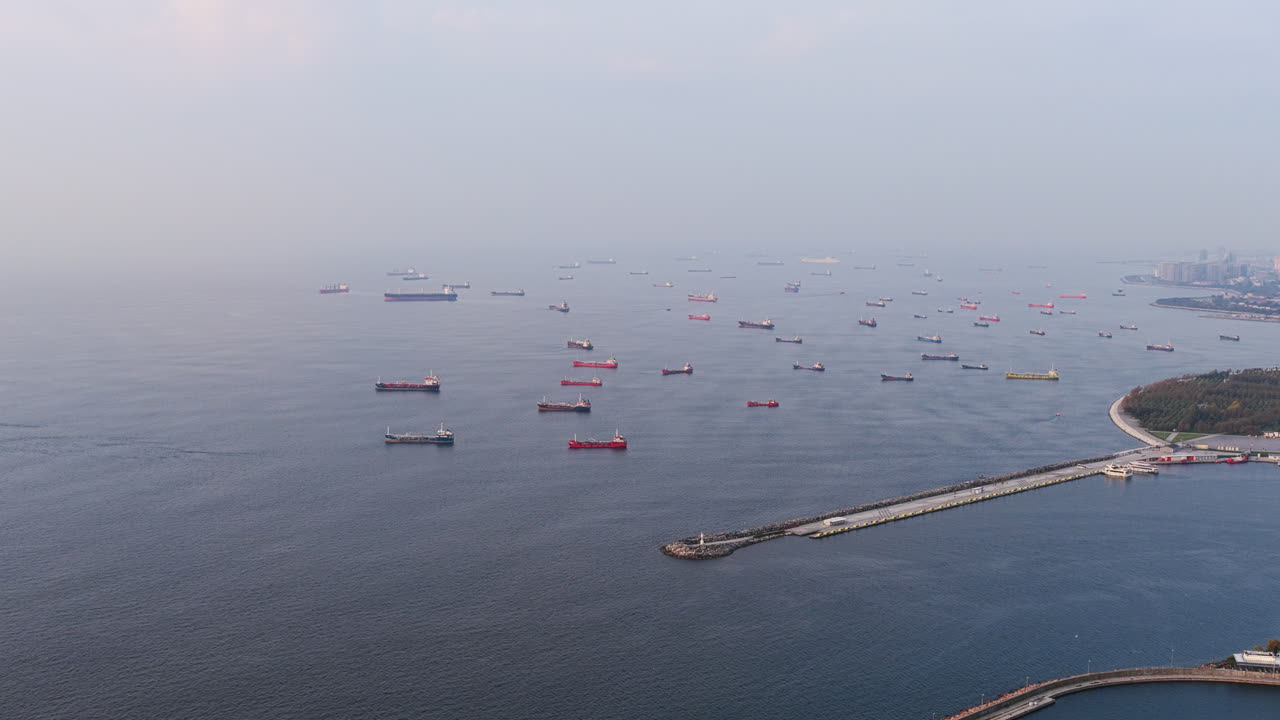 A wide aerial view of the Sea of Marmara filled with cargo ships, with the coastline and city infrastructure stretching along the shore
