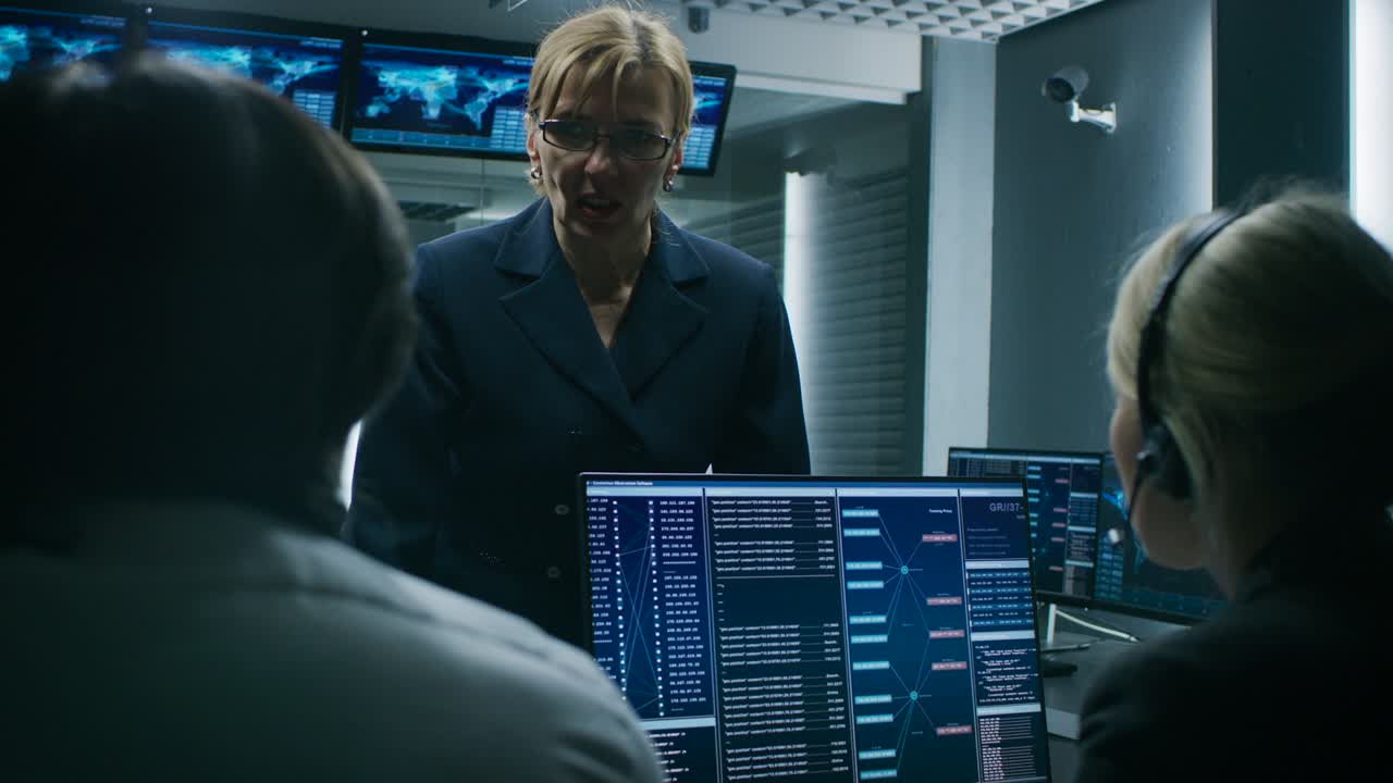 la jefa de operaciones habla con los despachadores de seguridad cibernética que trabajan en computadoras personales que muestran el flujo de datos de tráfico en la sala de control del sistema.
