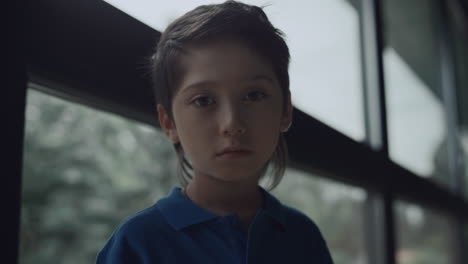 Portrait-upset-boy-looking-camera-near-panorama-window.-Schoolboy-posing-alone.