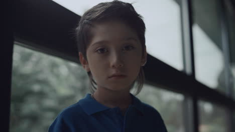 portrait upset boy looking camera near panorama window. schoolboy posing alone.