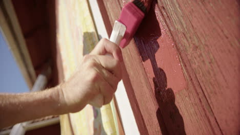 Exterior-wooden-wall-being-painted-traditional-falu-red-with-big-brush,-closeup