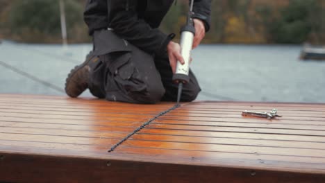 young man seals planked roof of wooden boat with sika flex waterproof mastic to seal out rain