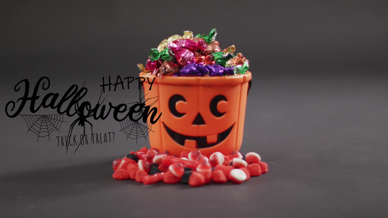 Happy halloween text banner with spider icon against pumpkin shaped bucket full of halloween candies