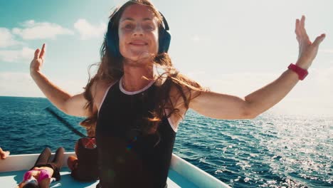 happy woman dances on the roof of a moving boat in headphones
